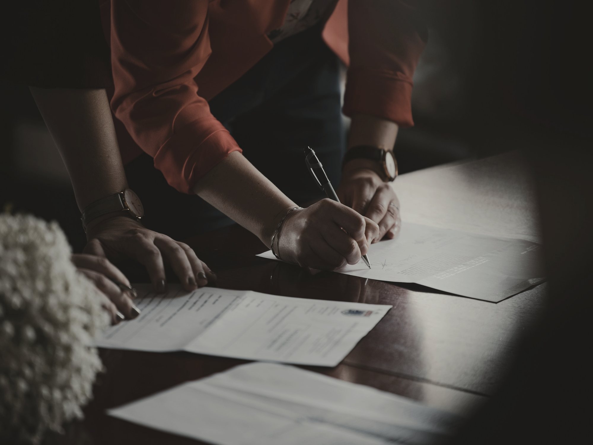 Hands signing a contract on a dark desk